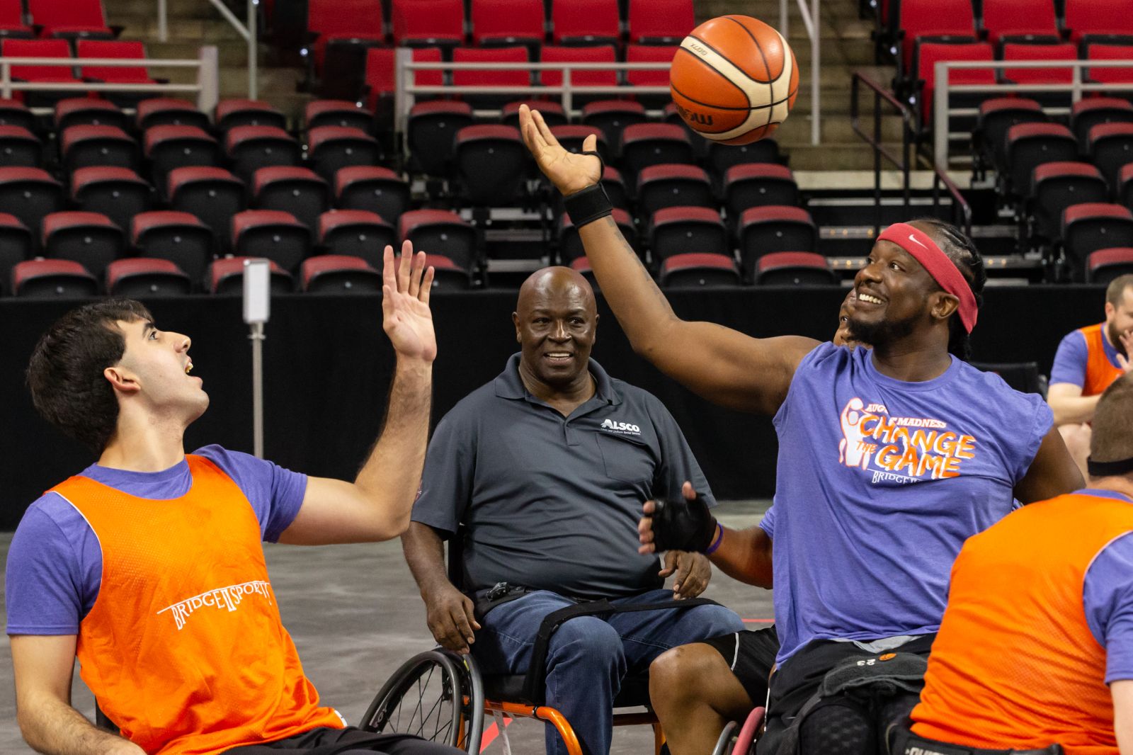 Two young men, one light skinned one dark skinned, in sports chairs compete for possession of a basketball.